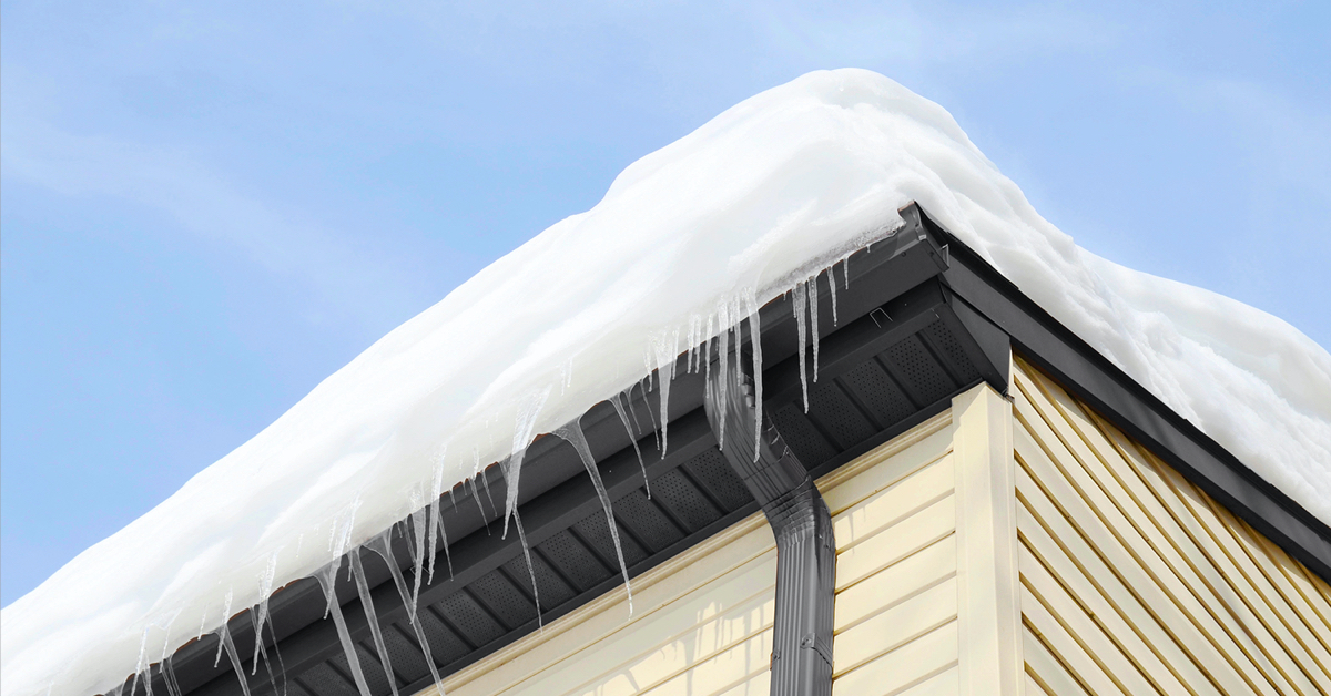 Neige épaisse et glaçons formant un barrage de glace au bord d’une toiture résidentielle, bloquant l’écoulement et favorisant les infiltrations d’eau.