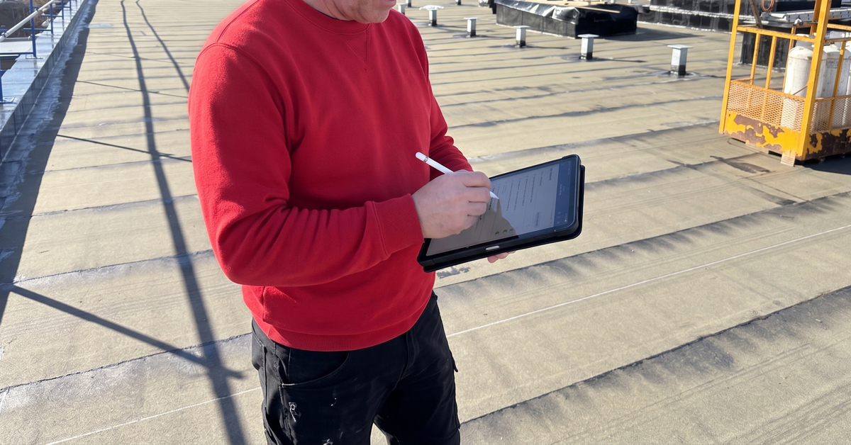 Technicien de toiture Aubin consignant sur tablette les résultats d’une inspection de toiture commerciale afin de documenter son état et les travaux requis.