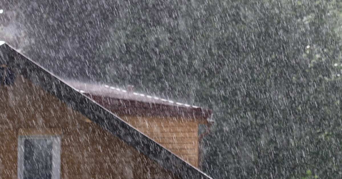 Pluie torrentielle s'abattant sur une toiture de maison avec gouttières, illustrant le risque immédiat de fuite de toiture et d'infiltration d'eau.