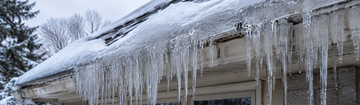 Glaçons massifs et accumulation de glace en bordure d'une toiture en hiver, signe d'un problème de ventilation d'entretoit.